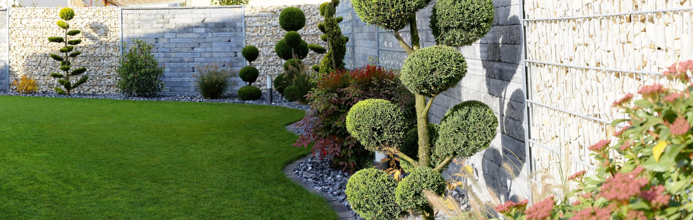 Jardin paysager moderne avec pelouse tondue, bordures végétalisées le long d'un mur en pierre naturelle