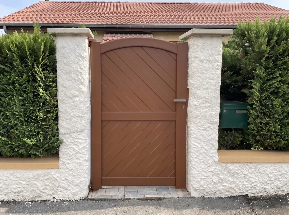 Scène extérieure résidentielle avec clôture en bois neuve longeant une pelouse verte bien entretenue, maisons en arrière-plan sous ciel bleu nuageux